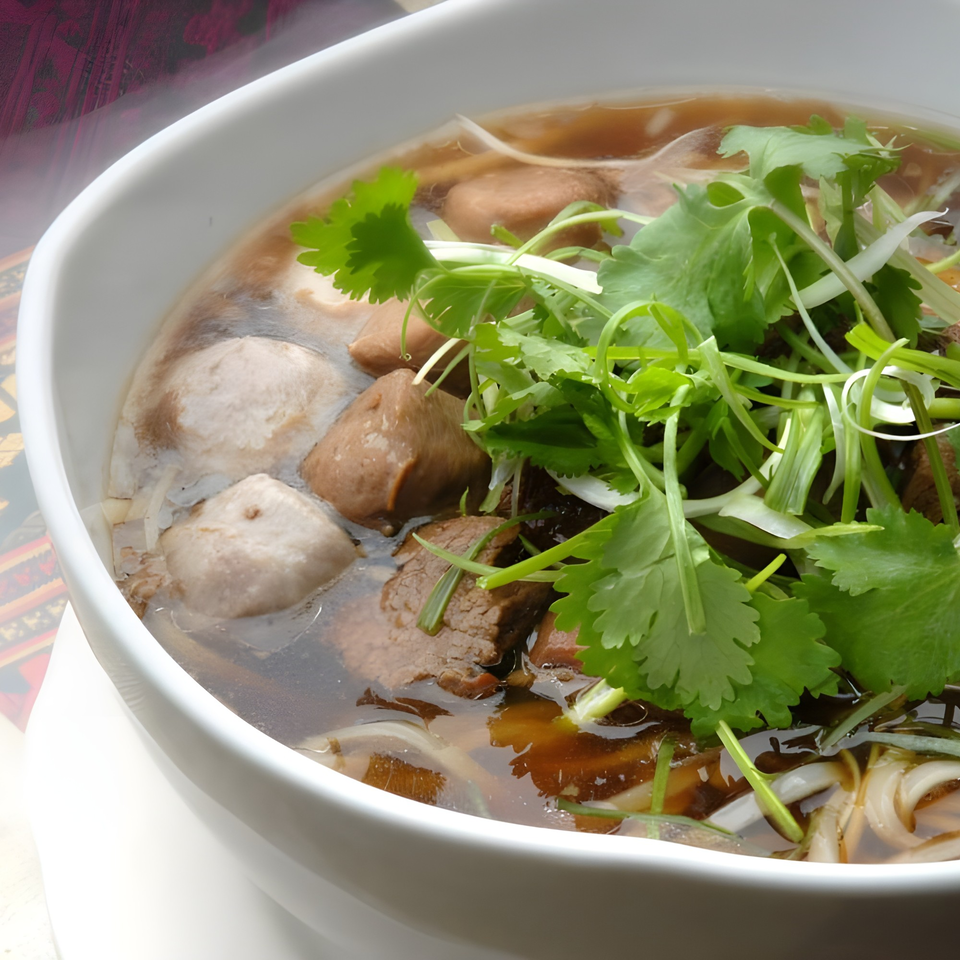 Close-up of a Thai noodle soup with beef, meatballs, and fresh cilantro in a white bowl.