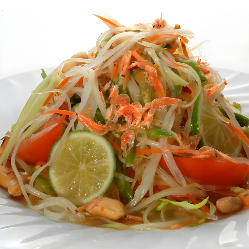 Close-up of a vibrant Thai papaya salad with shrimp, peanuts, tomatoes, and lime wedges.
